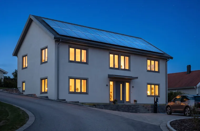 Svenskt hus i skymning med solceller på taket och tända fönster